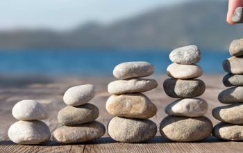 Hand making stacks of pebbles on wood background outside