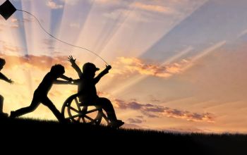 Enfant en fauteuil roulant qui s’amuse en faisant voler un cerf-volant avec d’autres enfants au coucher du soleil