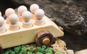 Toy wooden car with peg doll passengers outdoors.