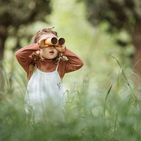 Child looking through cardboard tube binoculars while standing in tall grass.